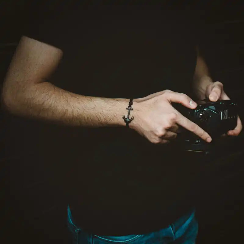 Un homme portant un bracelet ancre noir et tenant un appareil photo.